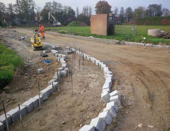 Bauarbeiten im Erschließungsgebiet Fahnbacher Straße Süd, Haiming, mit Bagger und Baustellenfahrzeugen.